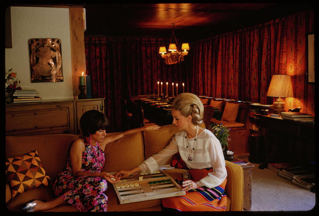 Two women playing backgammon on a sofa in a wood-panelled Swiss chalet, 1967